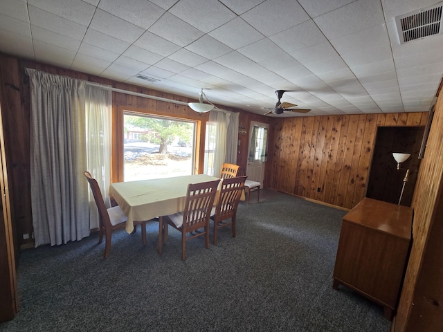 dining room featuring carpet floors, visible vents, and wooden walls