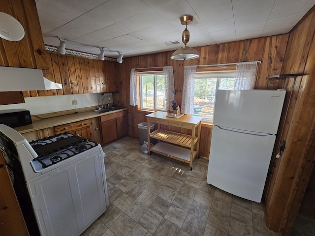 kitchen with black microwave, wooden walls, freestanding refrigerator, brown cabinets, and washer / clothes dryer