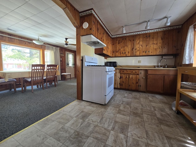 kitchen with under cabinet range hood, white range with gas cooktop, wood walls, and light colored carpet