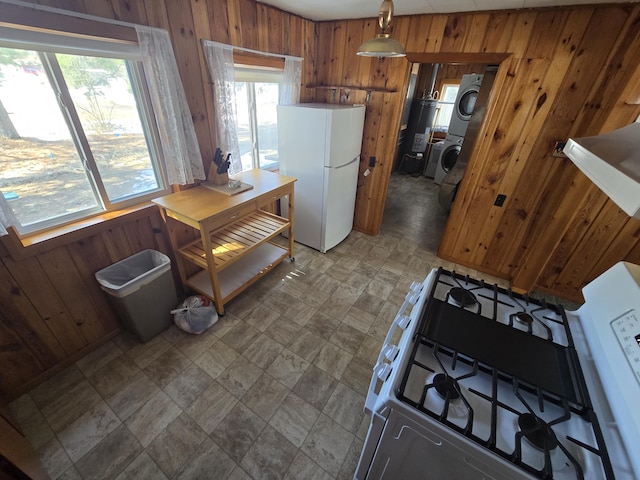 kitchen featuring white appliances, stacked washer / dryer, brown cabinetry, and wooden walls