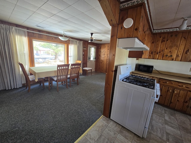 kitchen featuring black microwave, wooden walls, light colored carpet, under cabinet range hood, and gas range gas stove