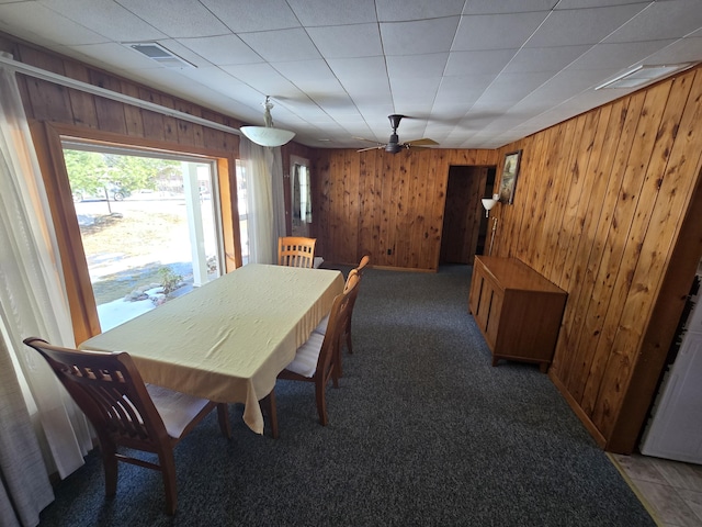 carpeted dining room with wood walls, ceiling fan, and visible vents