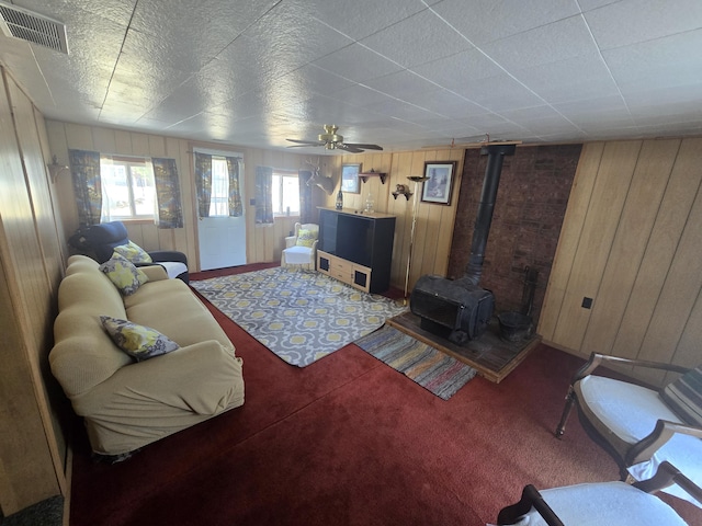 carpeted living room featuring a wood stove, visible vents, and ceiling fan