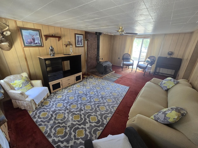 living area featuring a wood stove, wood walls, carpet, and a ceiling fan