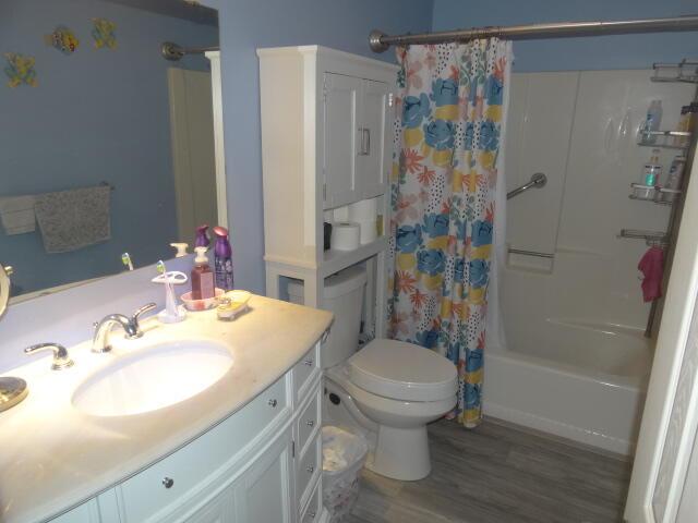 bathroom featuring shower / bath combination with curtain, vanity, toilet, and wood finished floors