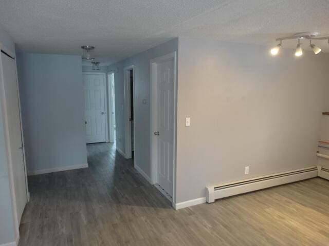 corridor with a textured ceiling, baseboards, baseboard heating, and wood finished floors