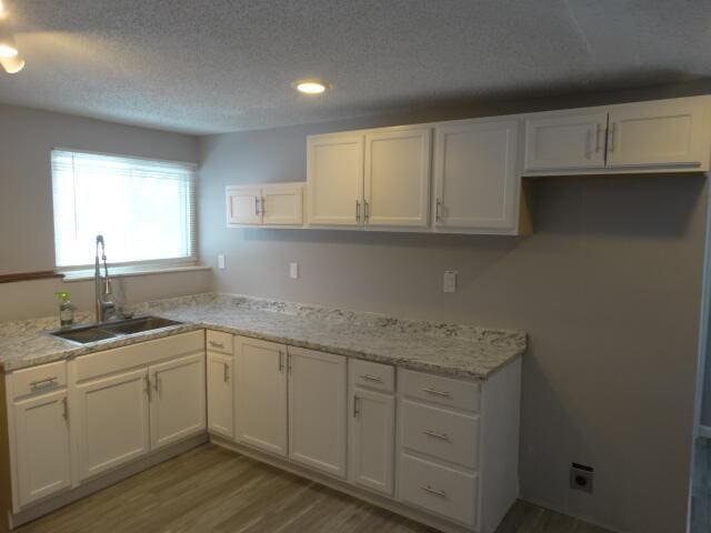 kitchen with a textured ceiling, white cabinets, a sink, and wood finished floors