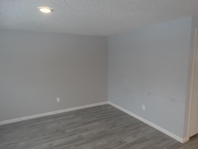 spare room with dark wood-type flooring, a textured ceiling, and baseboards