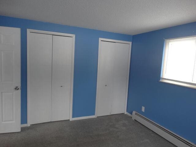 unfurnished bedroom with baseboards, baseboard heating, a textured ceiling, carpet floors, and multiple closets