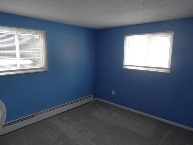 empty room with baseboards, a textured ceiling, a baseboard heating unit, and carpet flooring