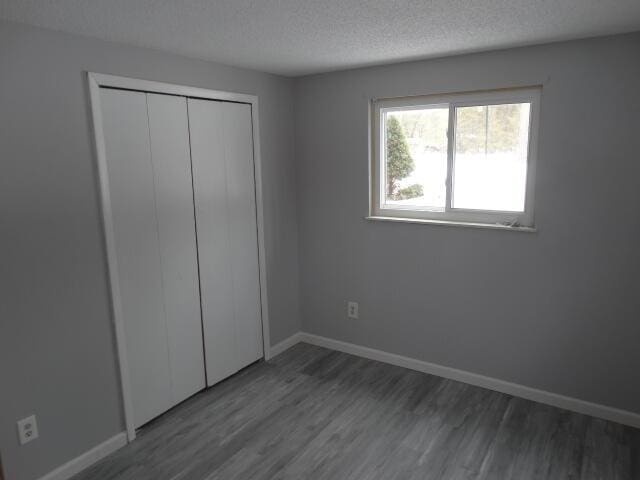 unfurnished bedroom with a closet, a textured ceiling, baseboards, and wood finished floors