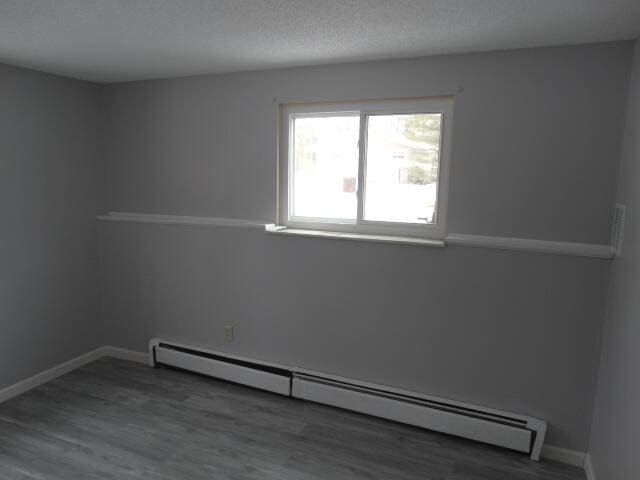 spare room with a baseboard radiator, a textured ceiling, baseboards, and wood finished floors