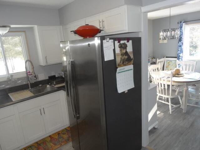 kitchen with stainless steel fridge, white cabinets, dark countertops, wood finished floors, and a sink