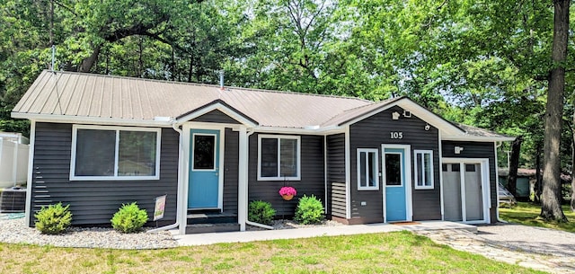 ranch-style home featuring central AC, metal roof, a garage, and a front yard