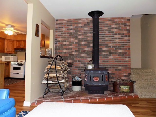 living room with ceiling fan, a wood stove, brick wall, and hardwood / wood-style floors