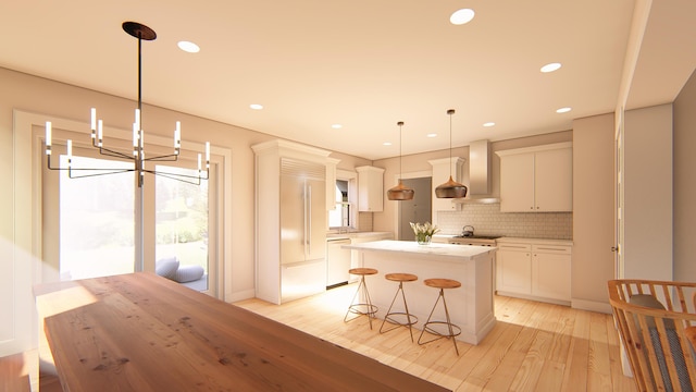 kitchen with decorative light fixtures, a center island, wall chimney range hood, white cabinets, and backsplash