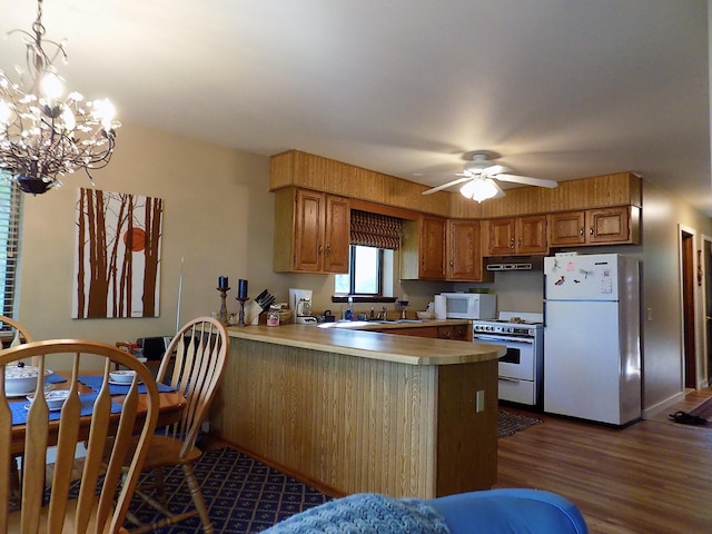 kitchen with dark hardwood / wood-style floors, kitchen peninsula, white appliances, decorative light fixtures, and ceiling fan with notable chandelier