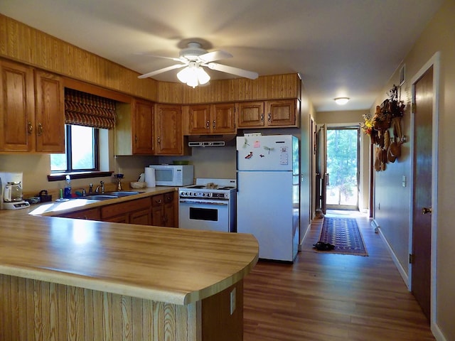 kitchen with dark wood-type flooring, kitchen peninsula, ceiling fan, white appliances, and sink