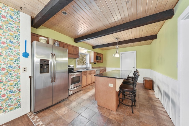 kitchen featuring appliances with stainless steel finishes, hanging light fixtures, a center island, beamed ceiling, and a kitchen bar