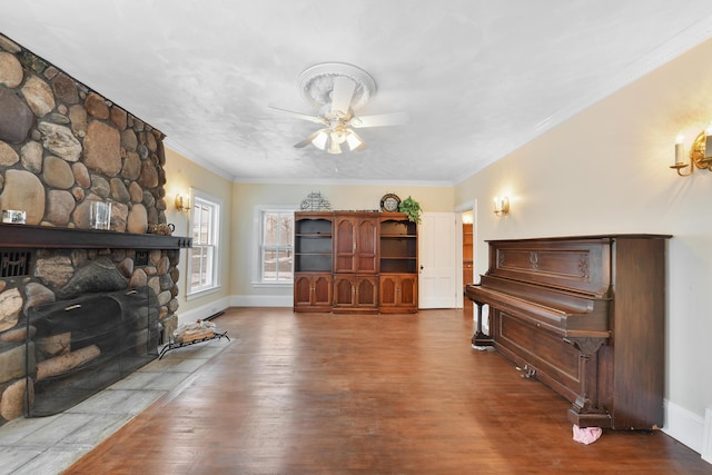 interior space featuring hardwood / wood-style floors, ornamental molding, ceiling fan, and a stone fireplace