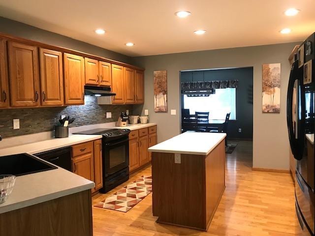 kitchen with a kitchen island, backsplash, light hardwood / wood-style floors, sink, and black appliances