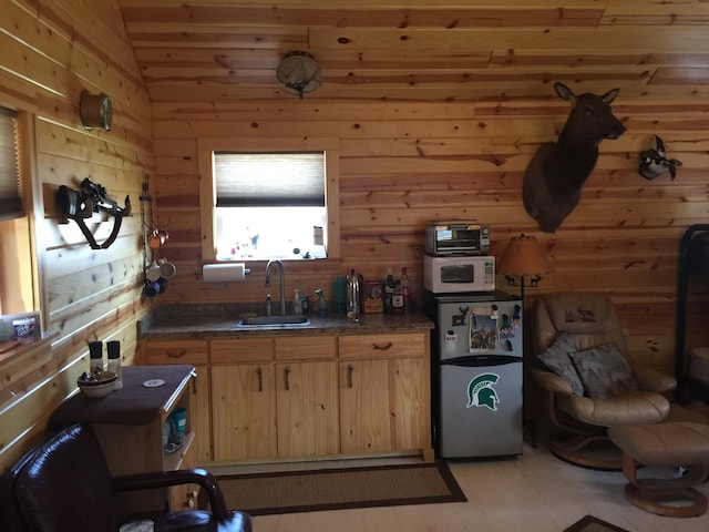 kitchen featuring light brown cabinets, wooden walls, lofted ceiling, stainless steel refrigerator, and sink