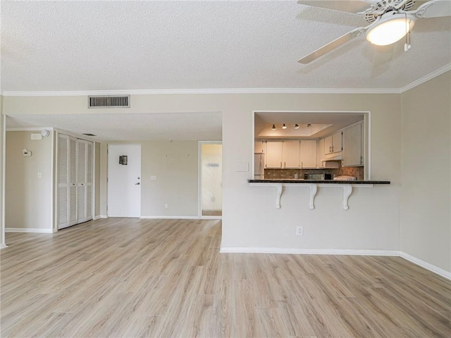 unfurnished living room featuring light wood-type flooring, a textured ceiling, ceiling fan, and crown molding