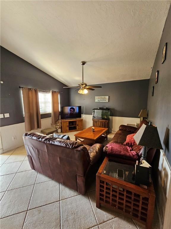 tiled living room featuring ceiling fan, vaulted ceiling, and a textured ceiling