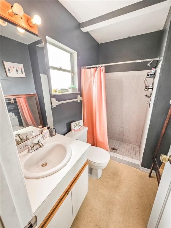 bathroom with walk in shower, vanity, toilet, and beamed ceiling