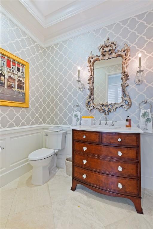 half bathroom with toilet, ornamental molding, vanity, and wallpapered walls