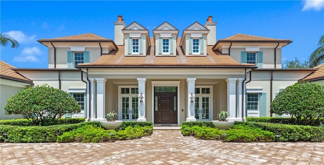 view of front facade featuring covered porch, french doors, stucco siding, a tile roof, and a chimney
