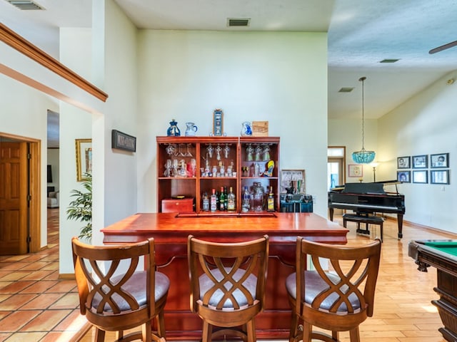 bar with pendant lighting, light hardwood / wood-style floors, a towering ceiling, and billiards