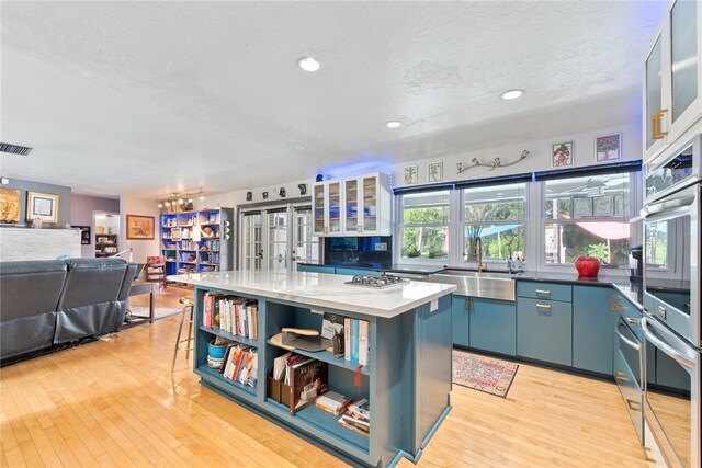 kitchen featuring blue cabinetry, sink, light wood-type flooring, and a center island