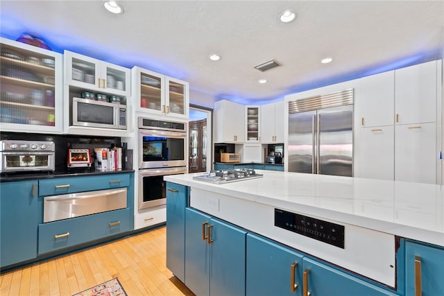 kitchen with stainless steel appliances, white cabinetry, dark stone counters, blue cabinetry, and light hardwood / wood-style flooring