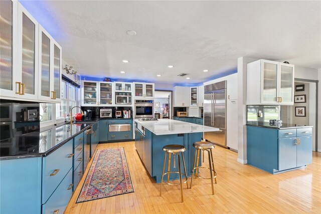 kitchen with white cabinetry, light wood-type flooring, stainless steel appliances, and a kitchen island