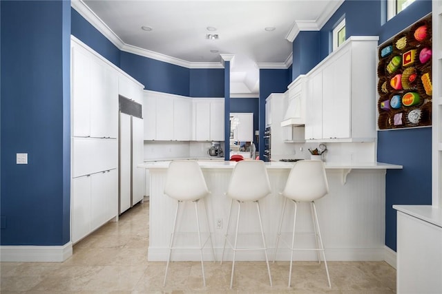 kitchen with white cabinetry, ornamental molding, a kitchen bar, and paneled built in refrigerator