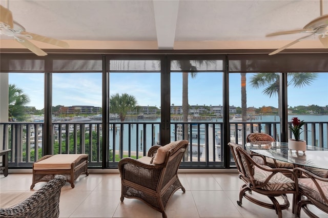 sunroom with ceiling fan and a water view