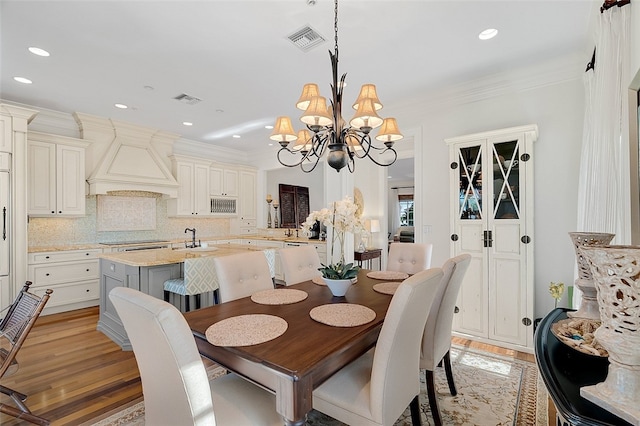 dining area featuring sink, light hardwood / wood-style flooring, ornamental molding, and an inviting chandelier