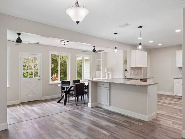 kitchen with a center island with sink, white cabinets, hanging light fixtures, sink, and light wood-type flooring