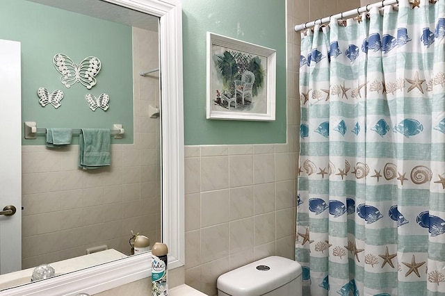 bathroom featuring toilet, a shower with shower curtain, and tile walls