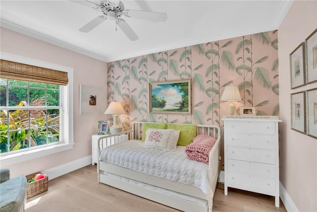 bedroom featuring baseboards, an accent wall, crown molding, wood finished floors, and wallpapered walls
