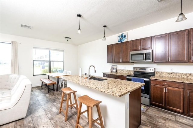 kitchen with sink, a breakfast bar, stainless steel appliances, a center island with sink, and decorative light fixtures