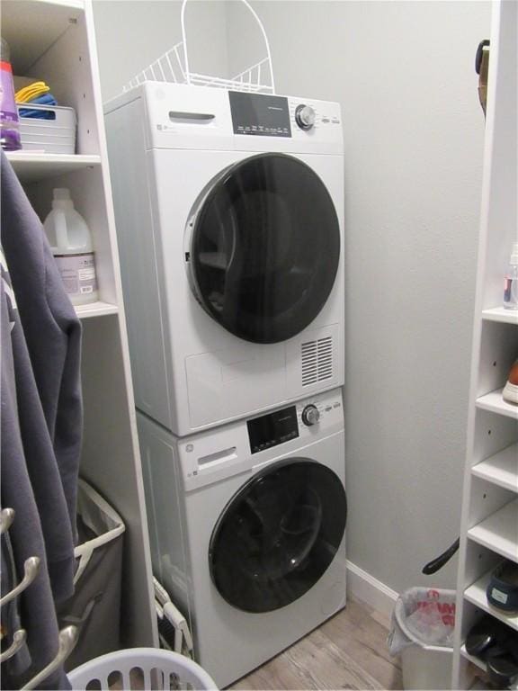 laundry room with stacked washer and dryer and light hardwood / wood-style flooring