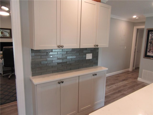 kitchen with dark wood-type flooring, tasteful backsplash, white cabinetry, and ornamental molding