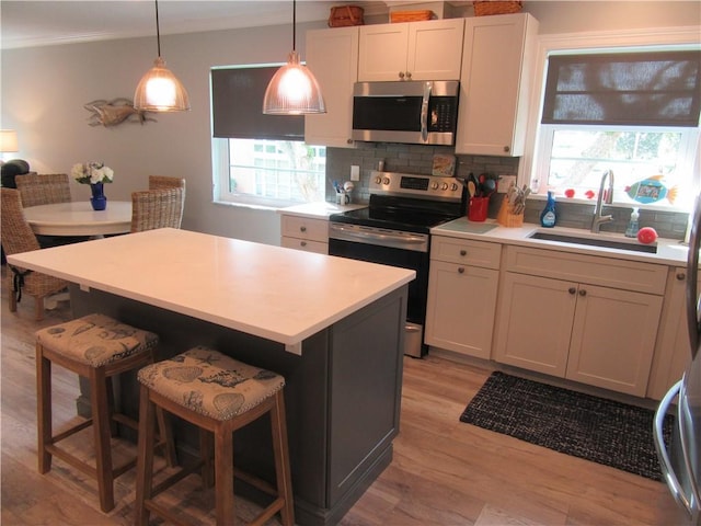 kitchen featuring appliances with stainless steel finishes, a breakfast bar, sink, white cabinets, and hanging light fixtures