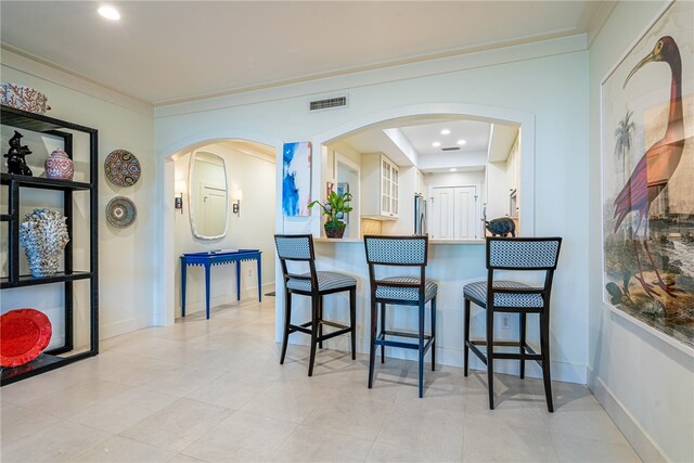 kitchen with a kitchen bar, light tile patterned floors, stainless steel fridge, and crown molding