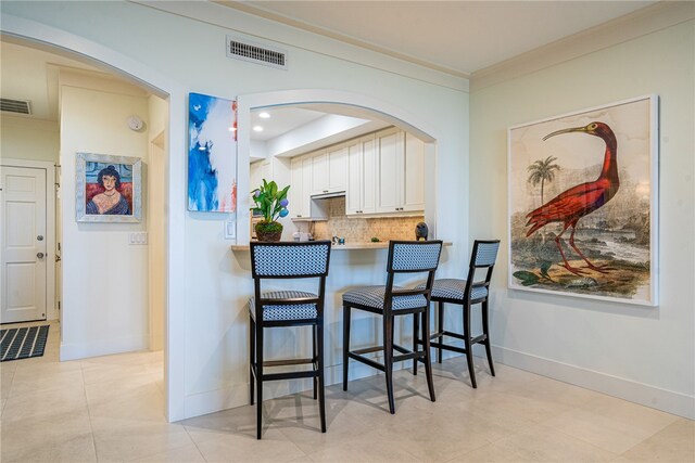 kitchen with kitchen peninsula, a breakfast bar area, light tile patterned floors, crown molding, and white cabinetry