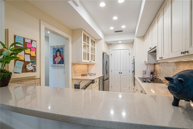 kitchen with stainless steel fridge, white cabinetry, backsplash, and light stone counters