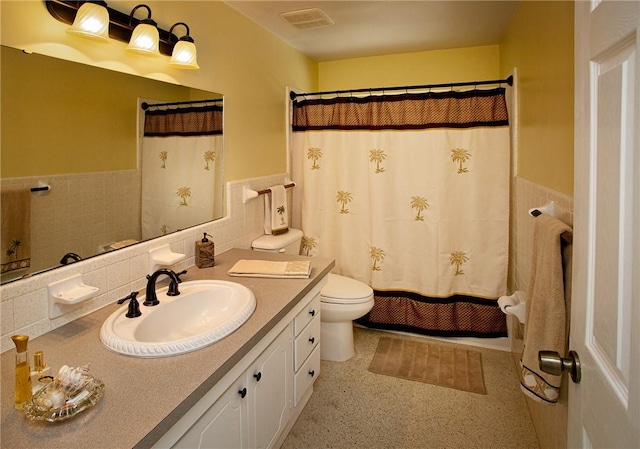 full bathroom with visible vents, toilet, tile walls, vanity, and a wainscoted wall