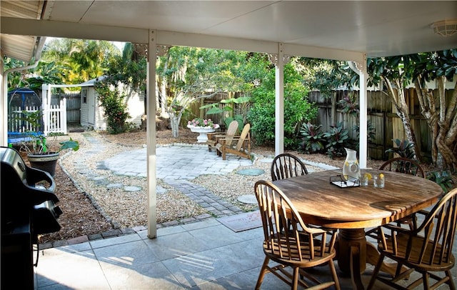 view of patio / terrace featuring an outbuilding, a fenced backyard, a storage unit, a trampoline, and outdoor dining area